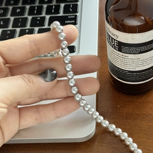 Détail d'un collier de perles grises lustrées tenu à la main dans un cadre de bureau