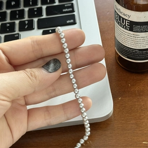 Détail d'un collier de perles gris argenté tenu en main pour montrer taille et texture