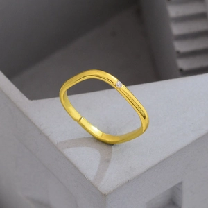 Minimalistischer quadratischer Goldring mit kleinem Zirkon auf grauem Steinhintergrund