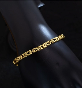 Vue macro d'un bracelet doré à mailles en écailles de dragon sur un support noir chic