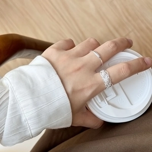 Set di anelli d'argento minimalisti con texture indossati su una mano con caffè caldo