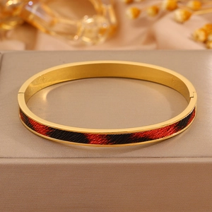 Dettaglio ravvicinato di un bracciale rigido in acciaio dorato con strisce rosse e nere