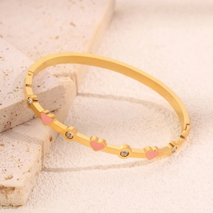 Dettaglio di un bracciale dorato con cuori in smalto rosa e pietre di zircone lucenti