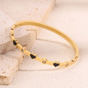 Dettaglio di bracciale cuore dorato con smalto nero e zircone su base di pietra
