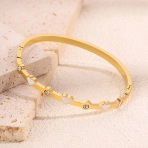Dettaglio macro del bracciale in titanio placcato oro con cuori bianchi e zirconi