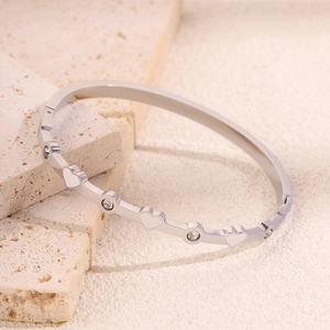 Dettaglio di smalto a cuore e cristalli su bracciale rigido in acciaio al titanio