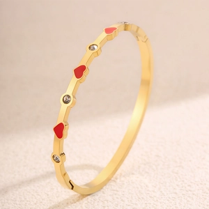 Dettaglio di un bracciale placcato oro con cuori in smalto rosso e cristalli incastonati