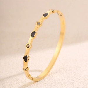 Dettaglio ravvicinato del bracciale rigido dorato con cuori in smalto nero e cristalli