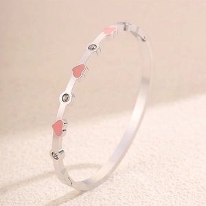 Dettaglio di un bracciale rigido con cuori in smalto rosa e pietre di zircone lucenti