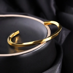 Detailed view of a golden Mobius twisted bangle on a black silk textured background