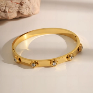 Detail shot of a polished gold titanium steel bangle featuring five crystal floral charms