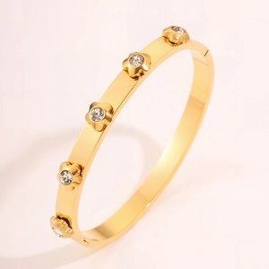 Detail of gold titanium steel bangle featuring five crystal inlaid flower charms and a polished finish