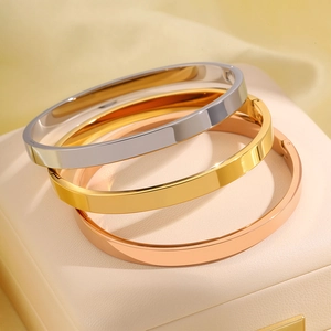 Detailopname van minimalistische platte armbanden in goud, zilver en roségoud op display