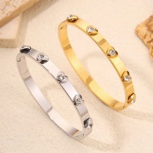 Gold and silver stainless steel heart bangles with clear crystals on sand background