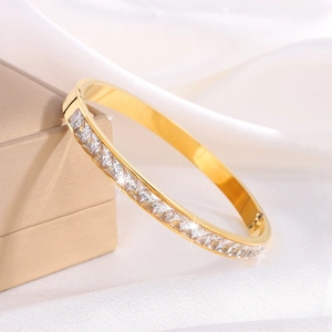 Dettaglio di un bracciale in titanio placcato oro con zirconi quadrati su sfondo di seta