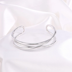 Primer plano de un brazalete abierto plateado de varias capas sobre fondo de seda blanca