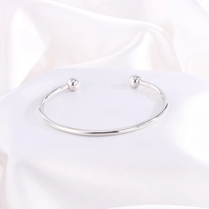 Vista macro de un brazalete abierto de acero pulido con cuentas sobre seda blanca