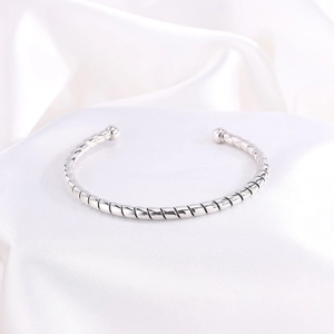 Brazalete rígido plateado minimalista con diseño trenzado sobre seda blanca