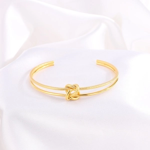 Detalle de brazalete abierto de doble banda bañado en oro de 18k con nudo sobre seda blanca