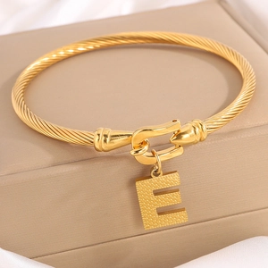 Detail van vergulde gedraaide titanium stalen armband met een getextureerde letter E hanger