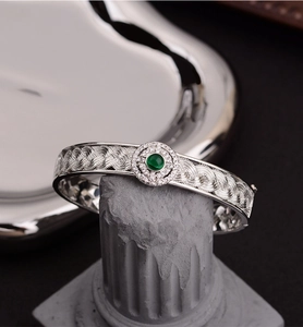 Macro shot of intricate braided texture and green emerald center on a silver retro bangle
