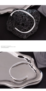 Dettaglio macro del bracciale rigido a goccia d'argento irregolare su sfondo roccioso