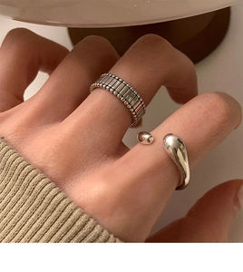 Detail of silver textured wide band and minimalist double ball open ring on finger