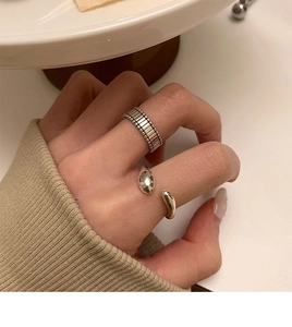 Detailed view of silver striped band and liquid-drop open ring on hand in warm natural light