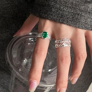 Elegante anello con gemma verde e design in piuma d'argento indossato su mano con maglione