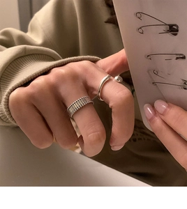 Detail view of silver textured band and open bead ring worn on hand for layered style