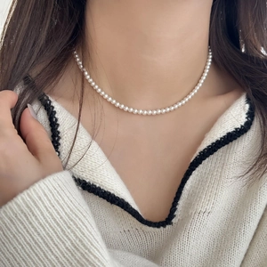 Gros plan d'un collier de perles blanches porté par un mannequin sur un pull beige