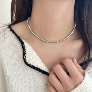 Gros plan d'un collier de perles argentées minimaliste porté par un mannequin au cou