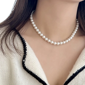 Élégant collier de perles blanches rondes porté sur un haut en tricot blanc au style chic