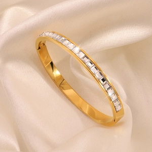 Elegant gold stainless steel bangle with row of rectangular zircons on silk background