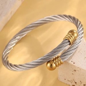 Gros plan d'un bracelet câble en acier torsadé avec embouts sphériques dorés polis