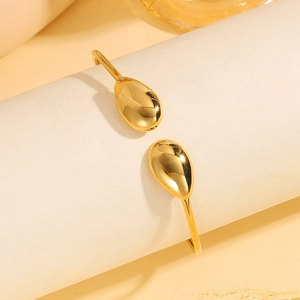 Close-up van een gouden roestvrijstalen open armband met druppelvormige uiteinden