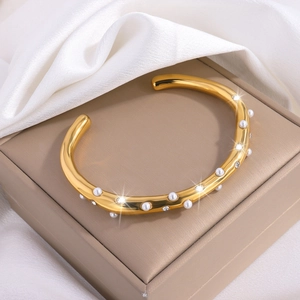 Macro-opname van gouden C-vormige armband met afwisselend parels en strassteentjes