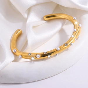 Detail van een vergulde cuff armband versierd met parels en ingelegde fonkelende strass