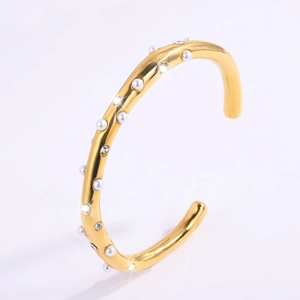 Detailopname van goud vergulde open armband met witte parels en schitterende strassteentjes