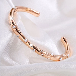 Detail van de roségouden open armband met witte parels en sprankelende kristalaccenten