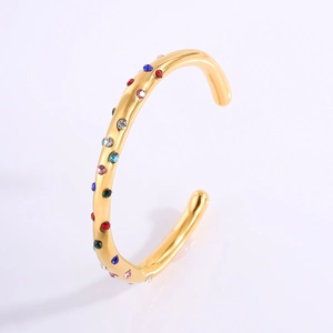 Detail van een goudkleurige roestvrijstalen C-armband met kleurrijke kristallen