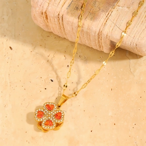 Detailed macro of golden four-leaf clover pendant with orange heart gems and white zircon