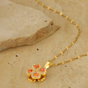 Macro detail of rotating four-leaf clover pendant with orange heart stones and 18k gold plating