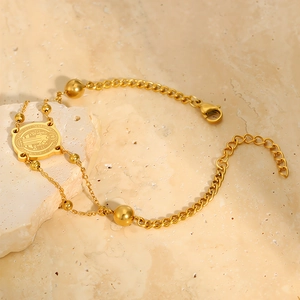 Detail eines goldenen Benedikt-Medaillen-Armbands mit Perlen auf einem Marmorhintergrund