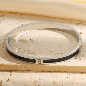 Macro view of silver-tone stainless steel bangle with black enamel and three inset zircons
