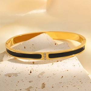 Macro detail of gold-plated bangle featuring black enamel inlay and three-stone setting