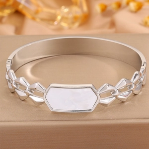 Detalle de brazalete de acero plateado con incrustación de nácar hexagonal y diseño geométrico