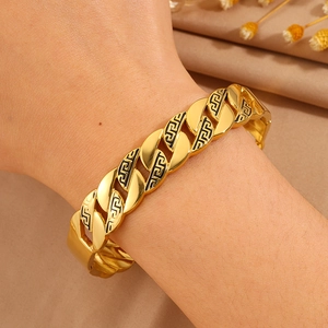 Detail eines goldenen Titan-NK-Kettenarmbands mit schwarzem geometrischem Muster am Handgelenk