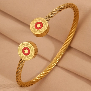 Détail d'un bracelet câble doré avec breloques étoiles en émail rouge sur tissu texturé