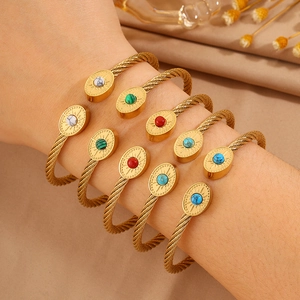 Détail de bracelets câbles dorés avec pierres ovales colorées sur le poignet d'un modèle